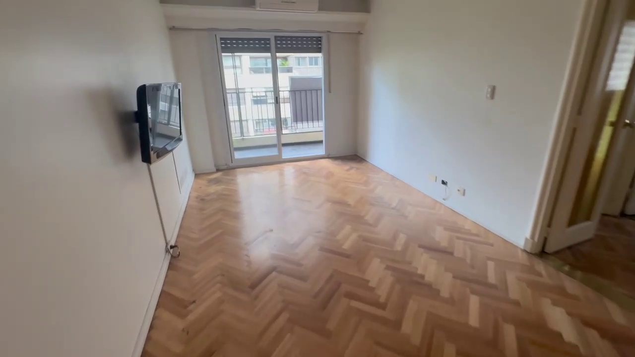 Empty living room with herringbone parquet floor and glass door to balcony