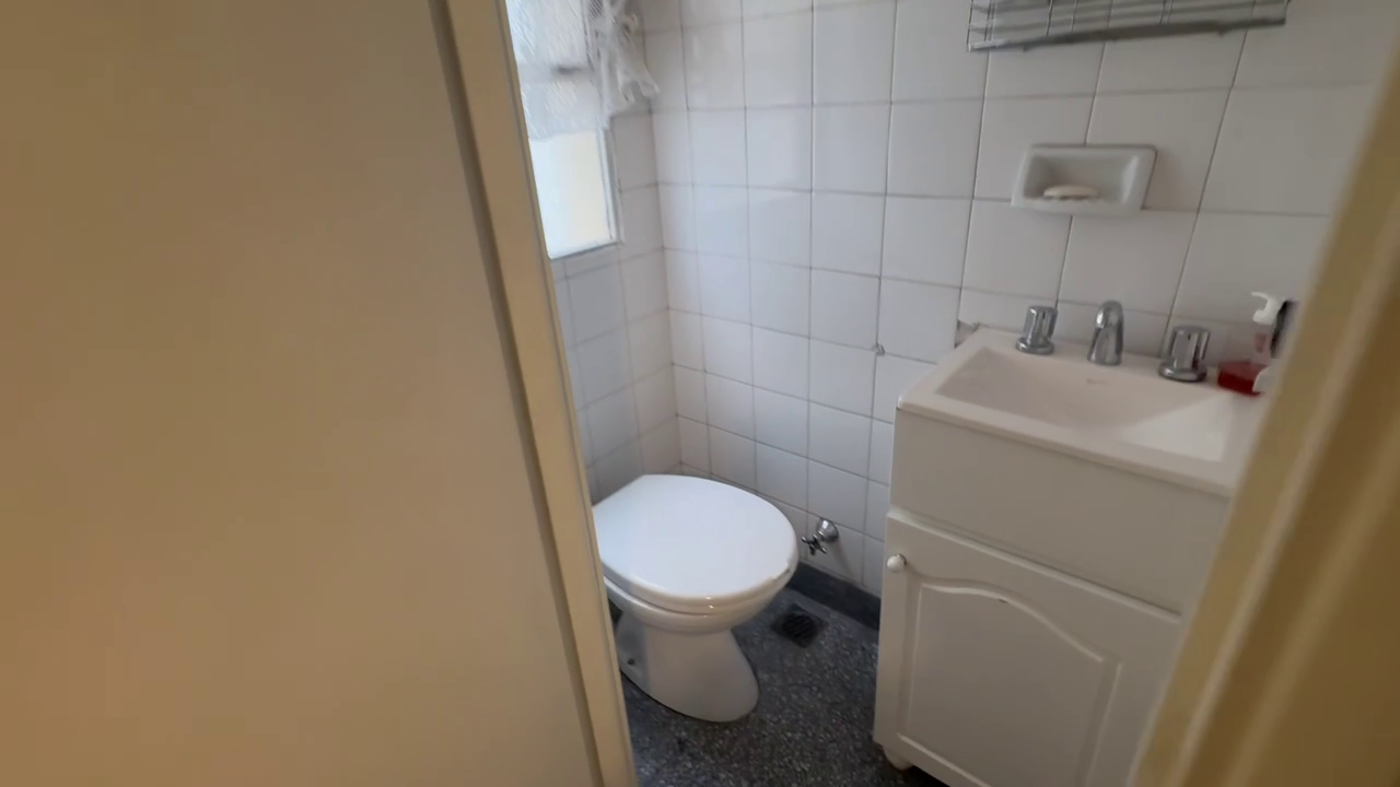 Small white-tiled secondary bathroom with toilet and pedestal sink