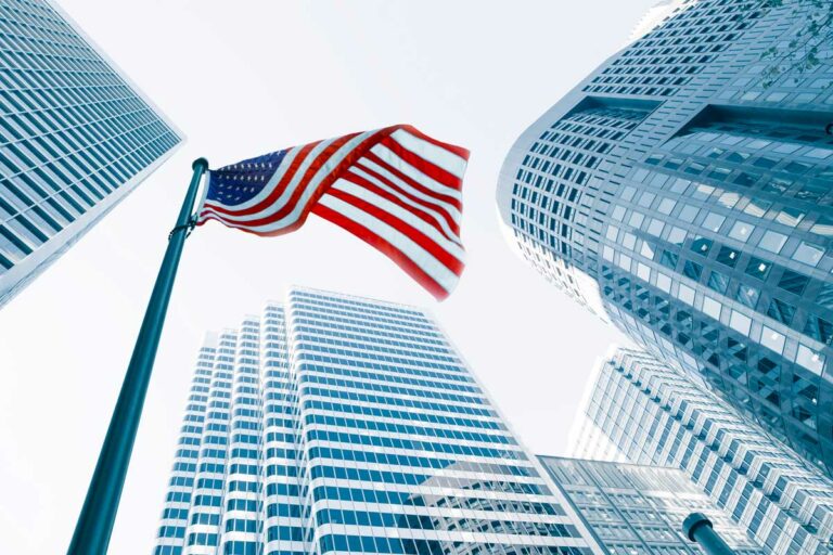 An American flag between two glass skyscrapers, looking up